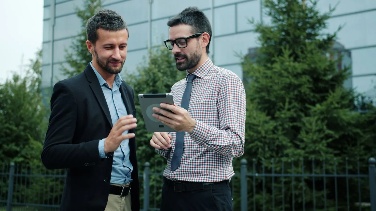 Two businessmen discussing work on a tablet in an outdoor setting.
